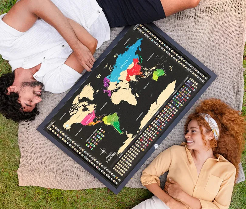 Casal deitado na grama ao lado do Mapa Mundi de raspar